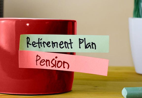 Cup of coffee on top of desk with sticky notes reading, retirement plan and pension.