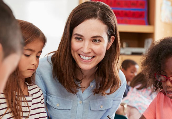 Young female teacher smiling as her students surrounded in the classroom